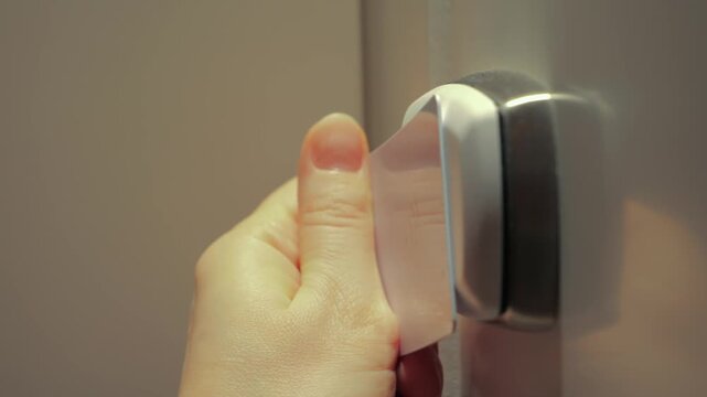 A close-up of a hand holding a hotel room key card and opening an electronic door lock. The scene illustrates modern access control systems, hotel services, and secure hotel room entry using RFID