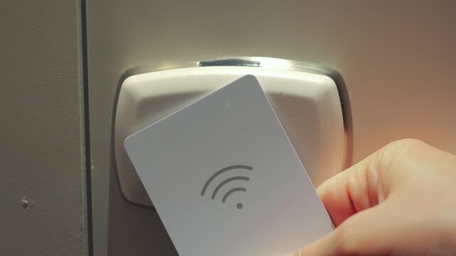 A close-up of a hand holding a hotel room key card and opening an electronic door lock. The scene illustrates modern access control systems, hotel services, and secure hotel room entry using RFID