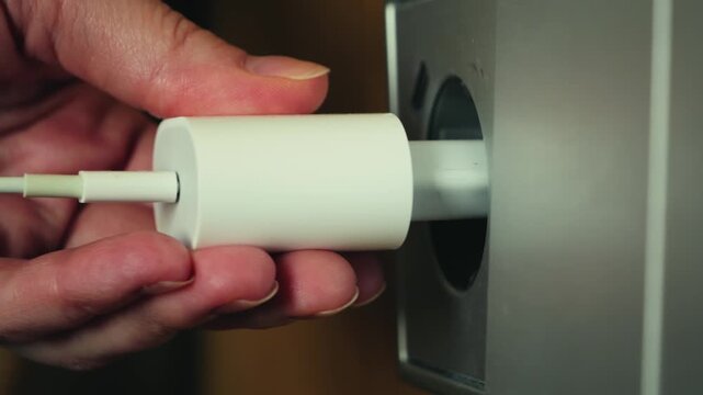 Close up of hand plugging charger into wall outlet, electricity usage and power connection concept. High quality 4k footage