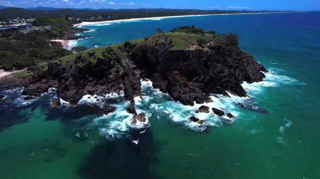 Aerial view of a rocky headland and inlet with crashing waves and turquoise sea