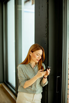 Woman using smartphone by window in a modern space during daytime