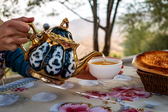 woman's hand pours hot tea into a bowl from a teapot