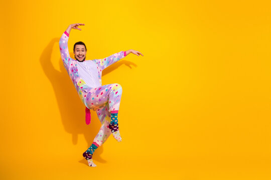 Happy man in colorful pajama jumpsuit performing playful pose against yellow background