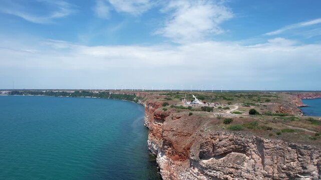 Aerial view of the rugged red cliffs of Kaliakra with wind turbines on the horizon and the blue waters of the Black Sea in Dobrich Province, Bulgaria.