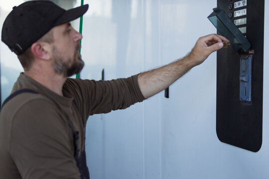 Man with beard and cap inserts a coin into a self-service car wash payment slot, starting the automatic cleaning cycle &mdash; quick, cash-based vehicle maintenance in an urban setting