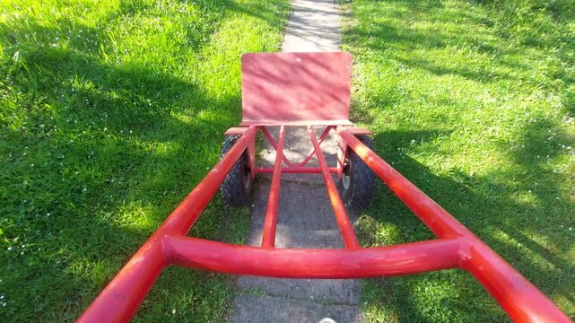 Moving empty red hand truck on garden path first person view