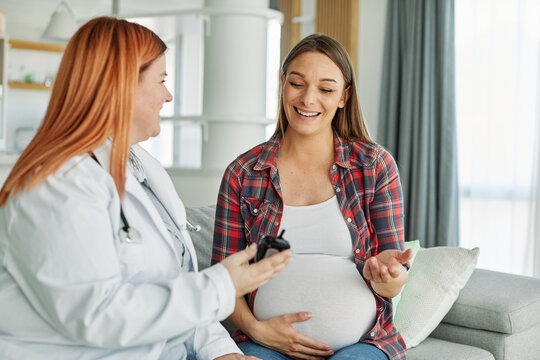 Portrait of a young happy pregnant woman doing exam with doctor or nurse during a visit at home or in a clinic