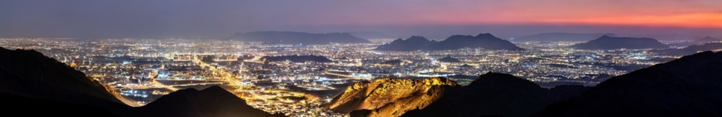 Fototapeta premium Wide panoramic night view of the illuminated city of Madinah in Saudi Arabia taken from the viewpoint at Jabal Uhud under a twilight sky.