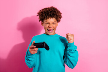 Excited young gamer celebrating a win while holding a game controller against a bright pink background © deagreez