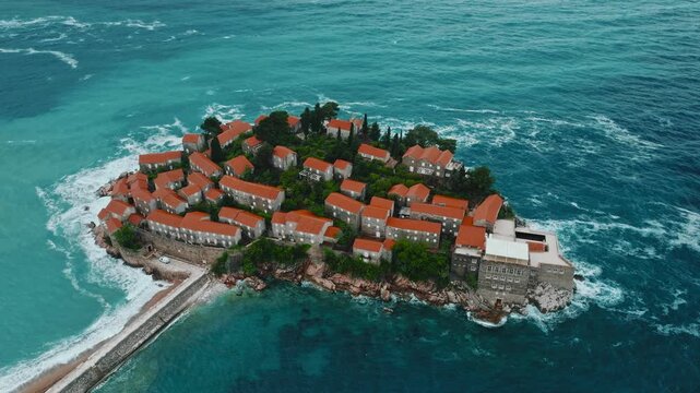 Cinematic aerial drone footage of Sveti Stefan featuring the iconic island village connected to the mainland by a narrow causeway, surrounded by turquoise Adriatic waters