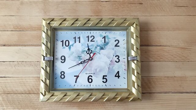 Square mechanical wall clock ticking on the wooden background