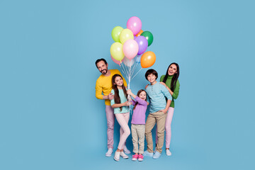 Fototapeta premium Happy family of five holding colorful balloons and smiling together against a blue studio background, parents and three children enjoying a cheerful celebration and playful moment