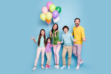 Fototapeta premium Happy family of five holding colorful balloons and smiling together against a pastel blue studio background, parents and three children in casual spring clothes celebrating a joyful moment