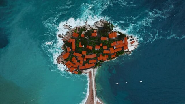 Cinematic aerial drone footage of Sveti Stefan featuring the iconic island village connected to the mainland by a narrow causeway, surrounded by turquoise Adriatic waters