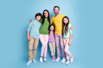 Fototapeta premium Happy family portrait of parents and three children standing together against a blue background, casual clothing and warm smiles showing togetherness, love, and modern family lifestyle