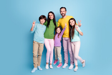 Fototapeta premium Happy family portrait of parents and three children smiling and making peace signs against a blue studio background