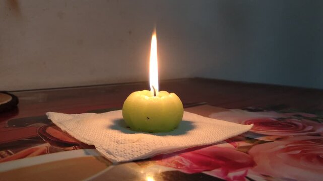 Burning pumpkin shaped candle on wooden table in dark cozy room