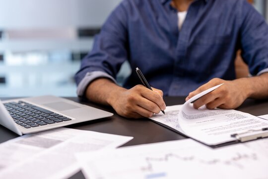 A close-up photo of a body part of a young man's hands signing documents at a desk in an office