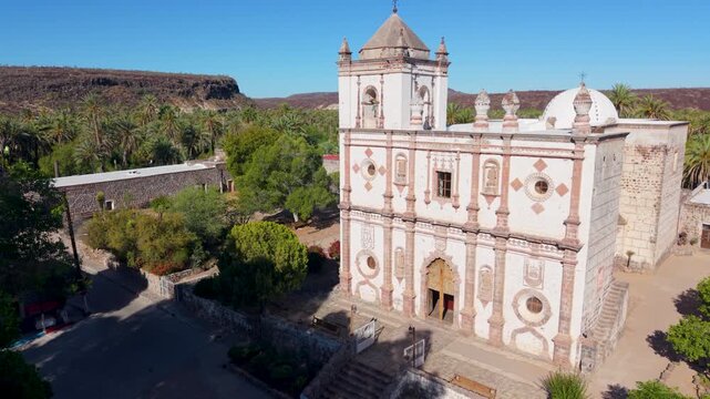 See aerial views of Mission Church located in San Ignacio, Baja California Sur, Mexico surrounded by the oasis and nearby buildings.