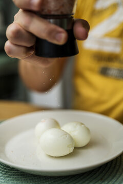 Boiled eggs for breakfast. Man's hand salting three boiled eggs in a plate. Eating proteins