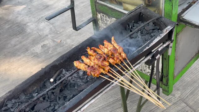 Traditional indonesian chicken satay being grilled over charcoal on a street food cart.