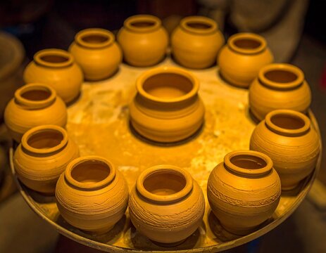 A close-up view of freshly made small clay pots arranged neatly on a circular tray, showcasing wet texture, smooth finishing, and traditional pottery craftsmanship in a workshop setting.