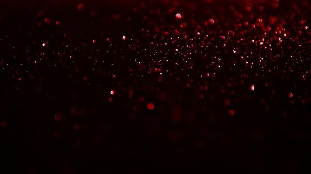 Close-up of sparkling red particles floating in dark space with dynamic motion
