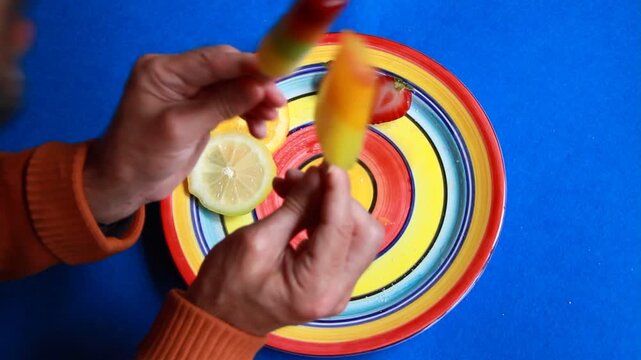 Comer y chupar dos helados de hielo polo de colores con palo sabor fruta pirulo ice cream fruit para refrescar verano y plato con c&iacute;rculos fantas&iacute;a con lim&oacute;n, naranja y fresa sweet summer y fondo azul