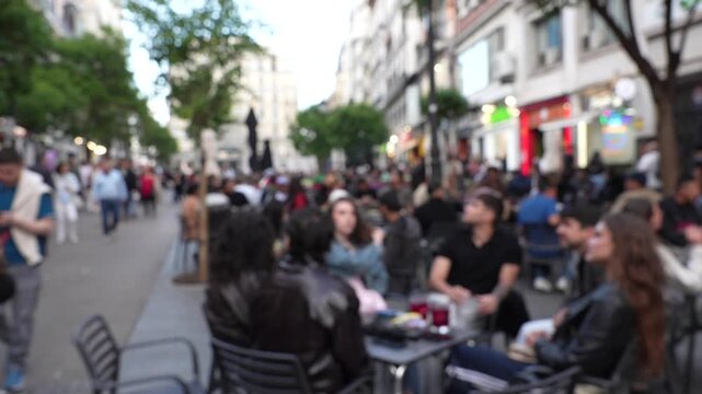 Defocused crowd of anonymous people relaxing and walking along a busy outdoor cafe street in central Madrid