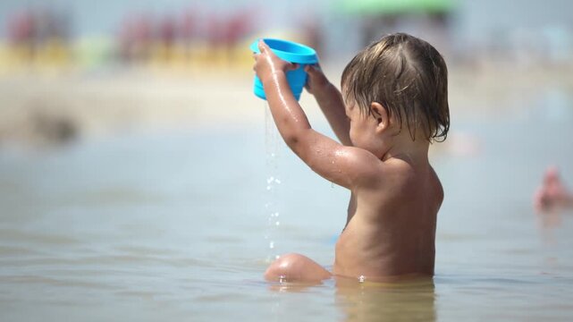 Kid collects shells and pebbles in the sea on a sandy bottom under the summer sun on a vacation