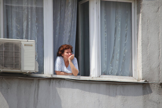 Senior woman coping with urban heatwave in apartment window
