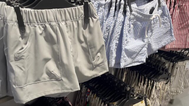 Panning shot of various casual summer shorts on hangers in a retail store.