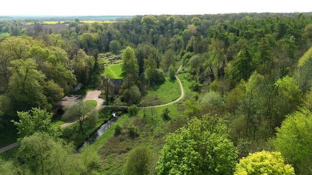 Aerial view of Roche Abbey ruins surrounded by dense woodland, a winding stream, and green meadows under soft daylight Maltby, England, United Kingdom.