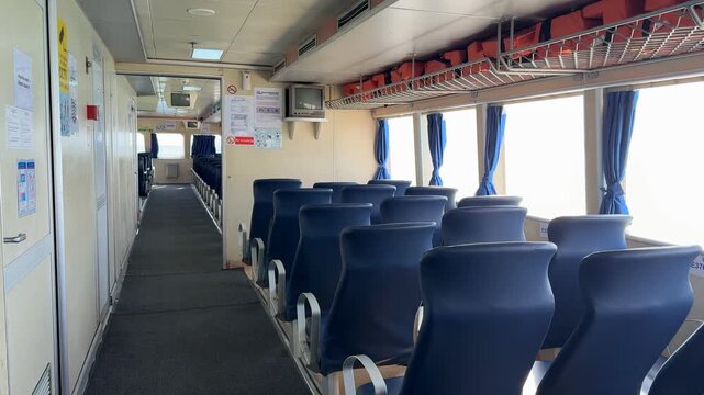 Empty ferry cabin with rows of blue seats and sunlight through windows, ideal for background