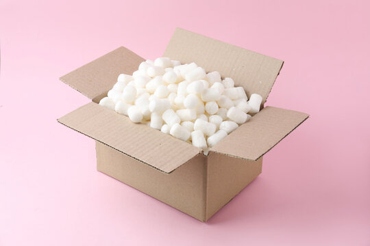 Cardboard box with styrofoam pieces and gift on pink background
