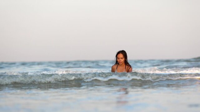 Girl with wet hair in a leopard swimsuit splashes water while sitting in the sea