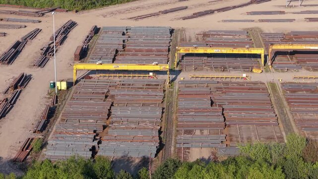 Aerial view of PD Ports industrial steel storage facility with yellow gantry cranes and stacks of metal beams under bright sunlight in Scunthorpe, England, United Kingdom.