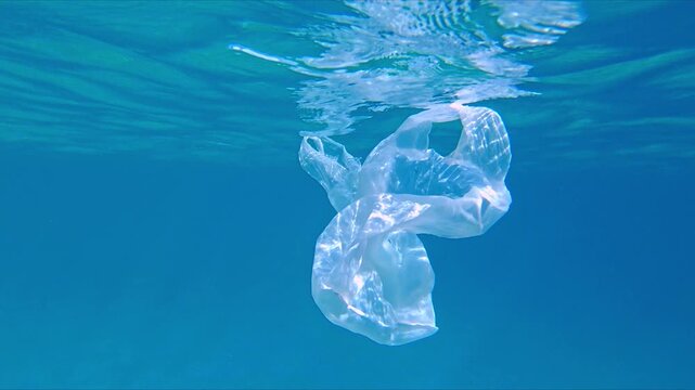 Close-up shot of a transparent plastic bag submerged in clear blue water, symbolizing pollution. The plastic's shape highlights its unnatural presence, illustrating environmental damage.