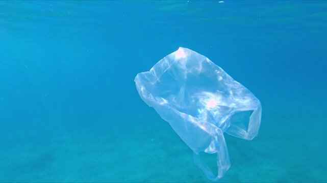 A plastic bag floats in clear blue ocean water, highlighting the issue of plastic pollution. The transparent bag contrasts with the vibrant underwater environment, emphasizing environmental damage.