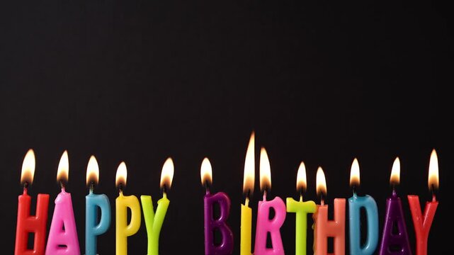 Birthday candles glow brightly against black background with copy space. Happy birthday greeting card.