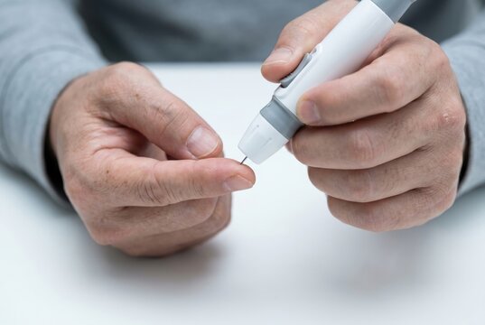 hands using lancing device on fingertip macro, blood glucose self-test diabetes monitoring