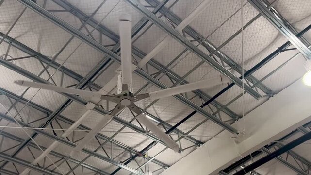 Large industrial ceiling fan in warehouse with metal rafters.