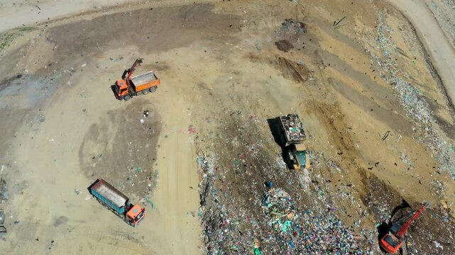 Brasov, Romania - 29 April 2026: Aerial view of trucks unloading waste at a landfill with birds flying over piles of garbage on a sunny day.