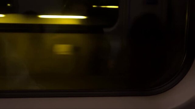 Subway train window tunnel lights flash rhythmic blur yellow grey abandoned station graffiti covered walls person reflection faintly visible interior motion, generative AI