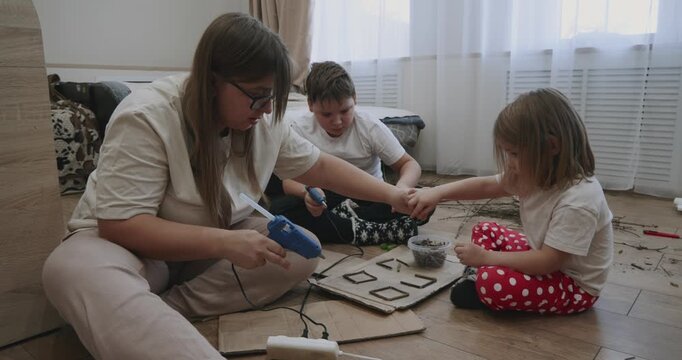 The creative family spends time at home, crafting with natural materials, cardboard, and a glue gun. The mother encourages the development of her children's creativity and fine motor skills.