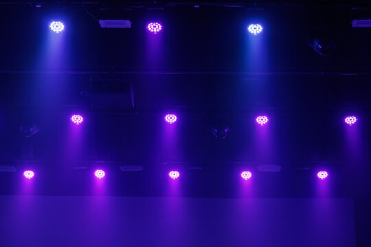 Purple and blue LED stage lights shine through haze from a dark ceiling rig, forming a moody concert background with copy space