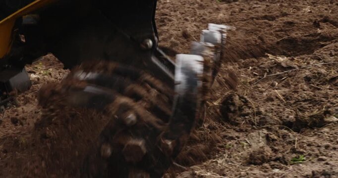 Close-up of a power tiller machine plowing the land and preparing the fertile soil for sowing seeds in a garden, with rotating blades digging and loosening the dark, rich earth.