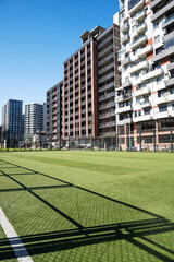 Urban football field beside tall residential buildings under clear sky. © Kufotos