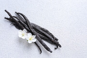Obraz premium Vanilla pods and flowers on white textured table, flat lay. Space for text