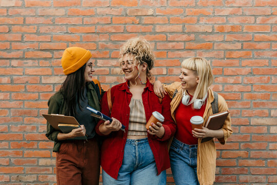 Diverse students smiling embracing on college campus brick wall